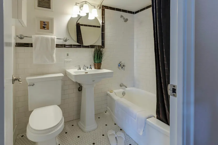 Before: small bathroom with white subway tile and black trim, a pedestal sink, a round mirror and a tub with a dark curtain