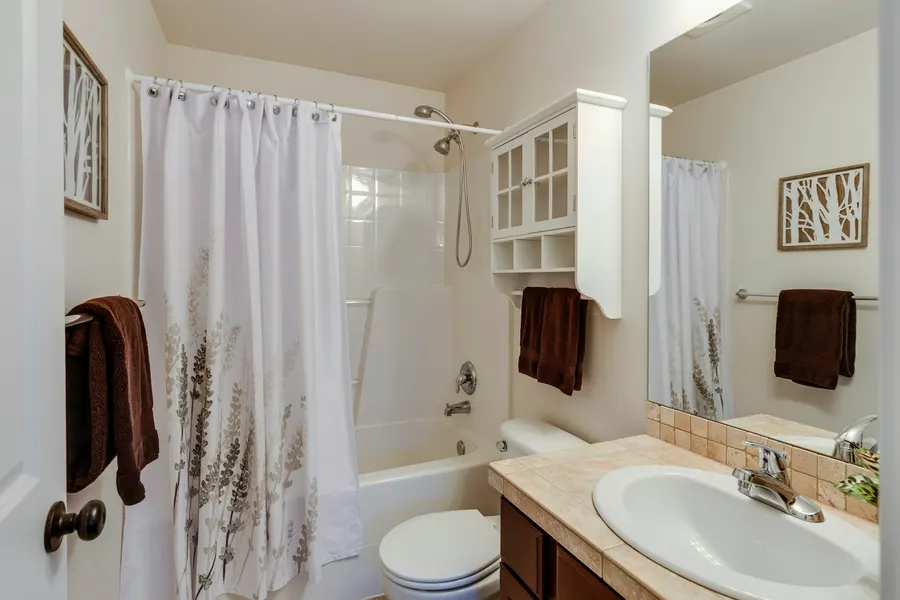 Before: builder-grade bathroom with beige walls, a leaf-print shower curtain and a dark wood vanity