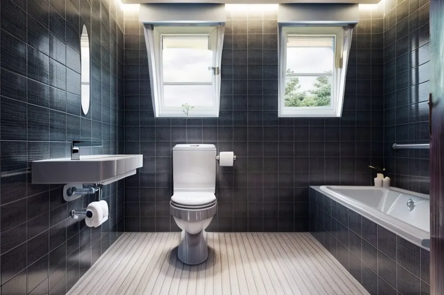 After: the same bathroom in minimalist style with large charcoal tiles, a slim wall-hung sink, a white tub and hidden cove lighting