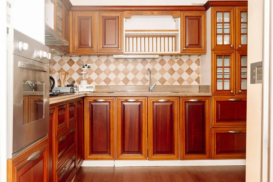 Before: kitchen with glossy cherry-wood cabinets, a beige granite counter and a diamond-pattern tile backsplash