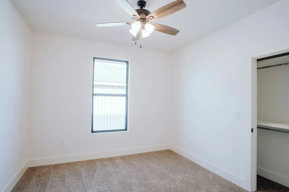 Before: an empty bedroom with white walls, beige carpet, one window, a ceiling fan and an open closet