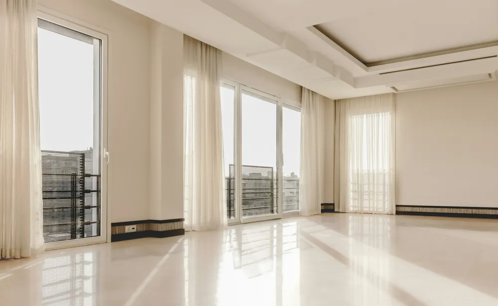 Before: a large empty living room with a white marble floor, tall windows and sheer curtains