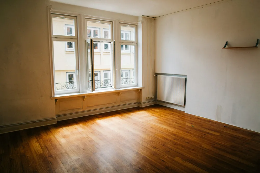 Before: an empty living room with three tall windows, a radiator and a plain wall