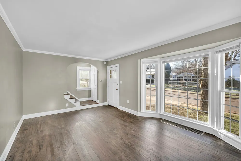 Before: an empty living room with grey walls, dark hardwood floor and a bay window