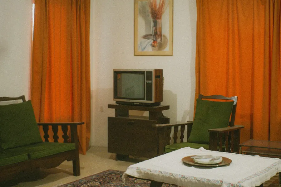 Before: dated living room with bright orange curtains, green wooden chairs and a tube TV