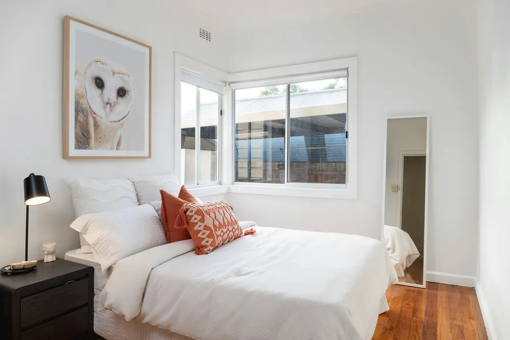 Before: a small white bedroom with a corner window and a tall mirror