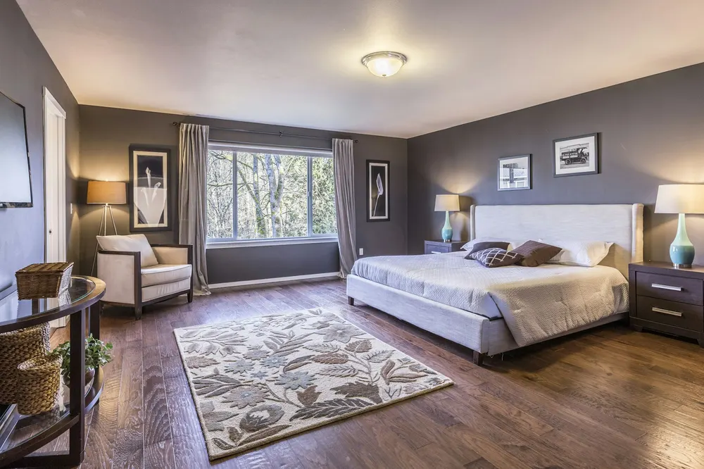 Before: a large master bedroom with dark grey walls, a patterned rug and an upholstered bed