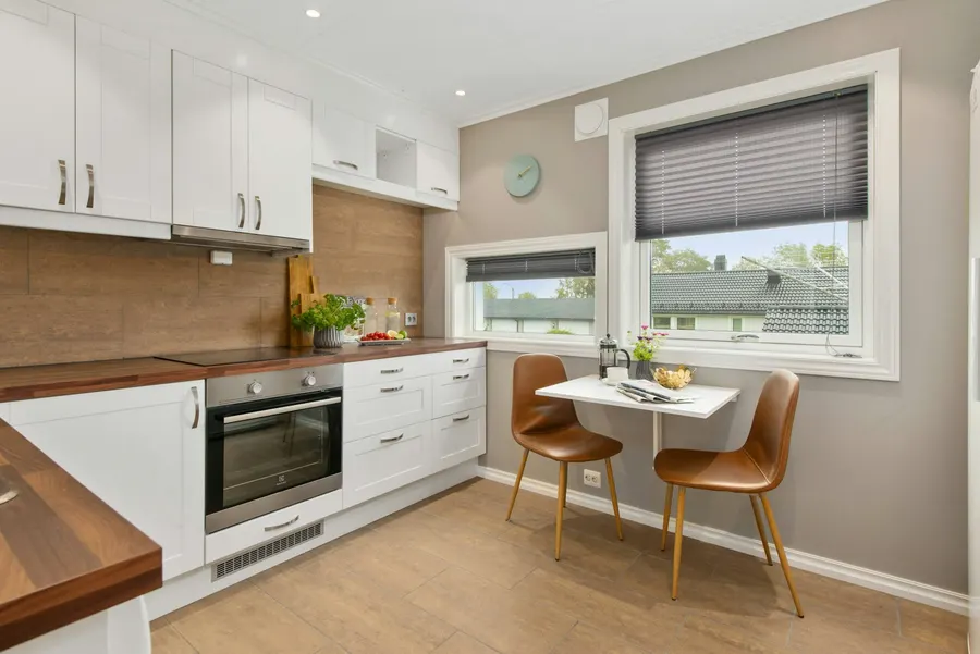 Before: bright kitchen with white shaker cabinets, a brown tile backsplash, taupe walls and a small dining table