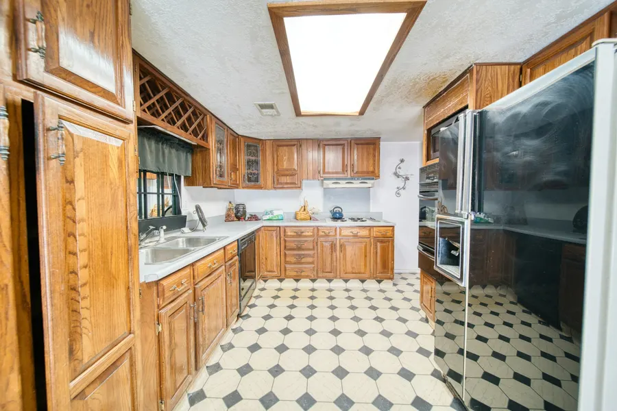 Before: dated U-shaped kitchen with oak cabinets, white laminate counters, a black-and-white vinyl floor and a fluorescent ceiling light