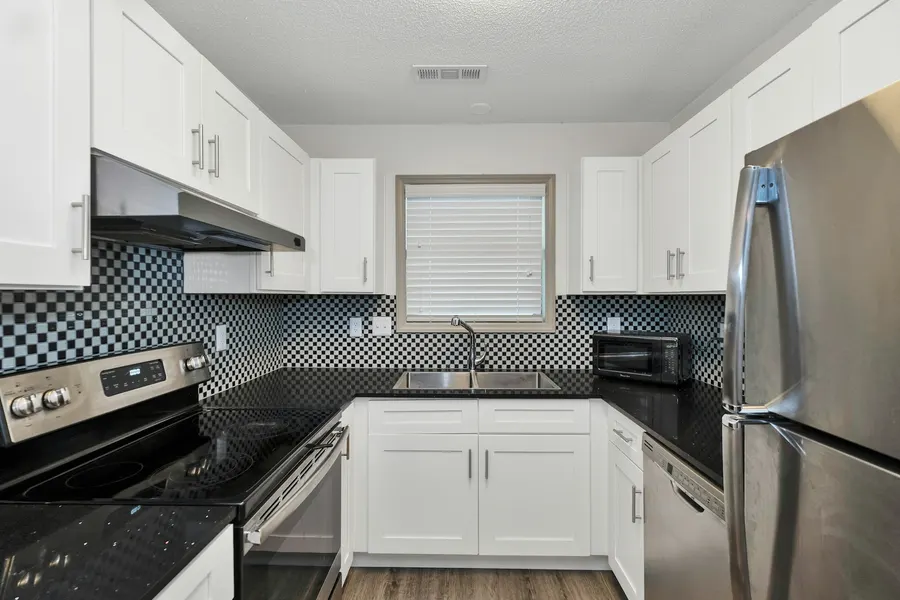 Before: rental U-shaped kitchen with white shaker cabinets, black granite counters and a black-and-white checker mosaic backsplash