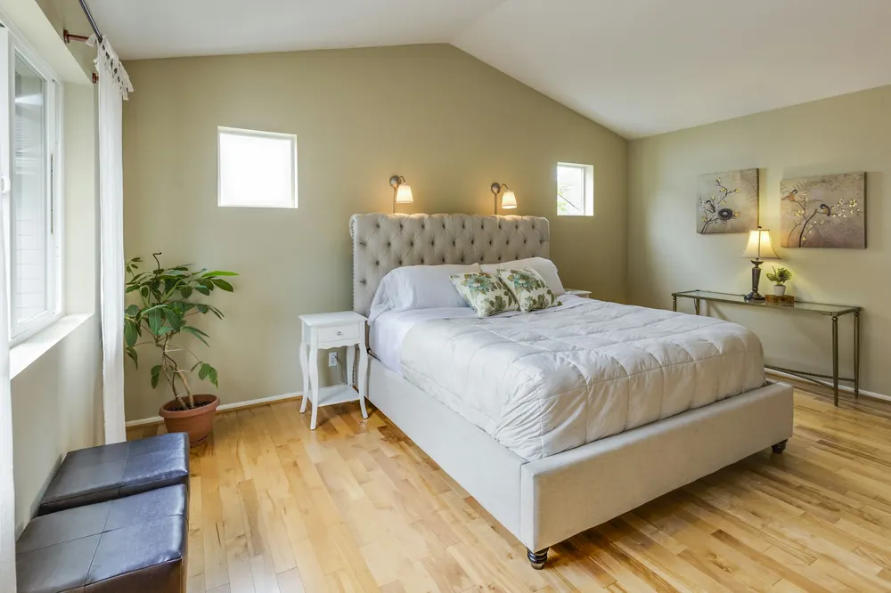 Before: a bedroom with a vaulted ceiling, sage walls, a tufted bed and a plant by the window