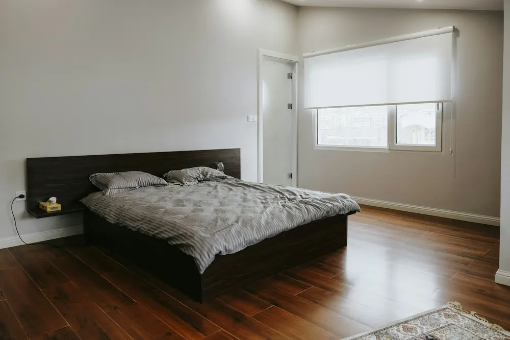 Before: a simple bedroom with a black bed, a dark wood floor and a blind over the window