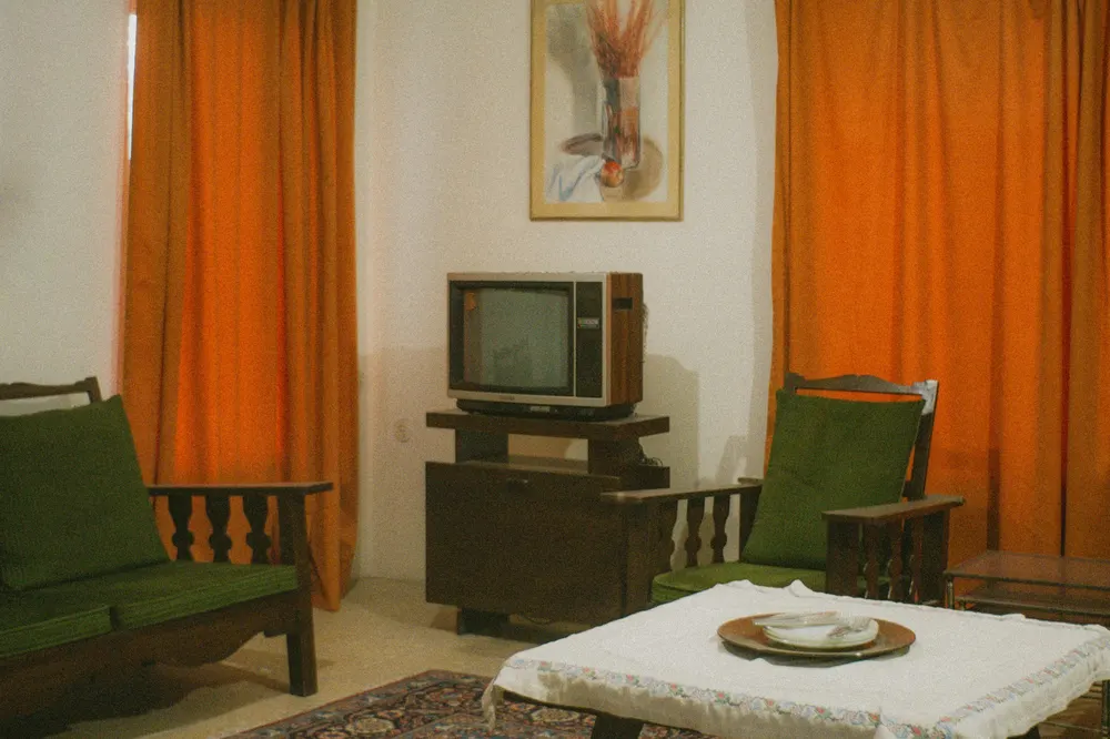 Before: a 1970s living room with orange curtains, green armchairs and an old TV