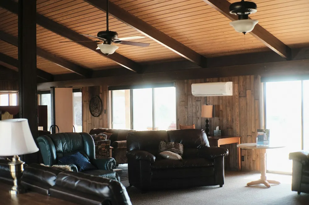 Before: a dark living room with black leather sofas, a beamed ceiling and a wood-panelled wall